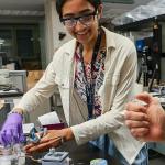 smiling student in a white lab coat and safety glasses handling equipment in a lab